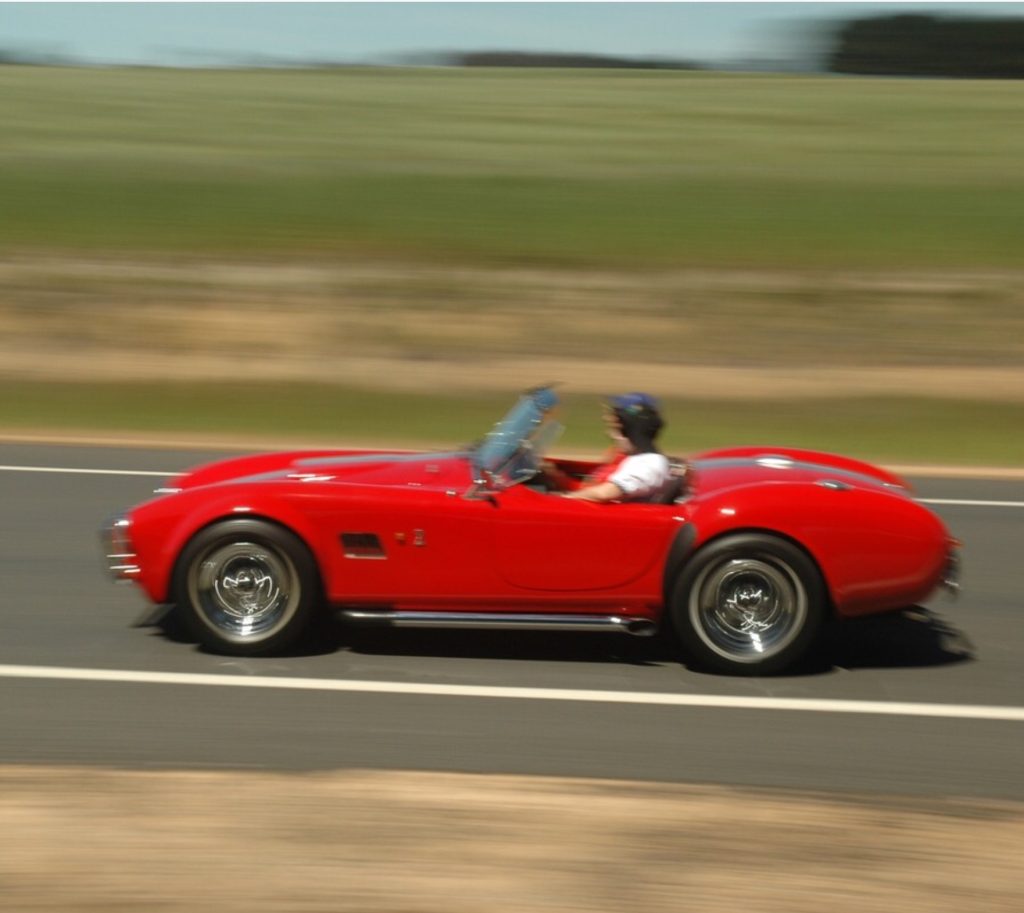 A red Cobra speeds along the West Wyalong disused runway, the fields in the background are out of focus suggesting how fast the vehicle is moving.
